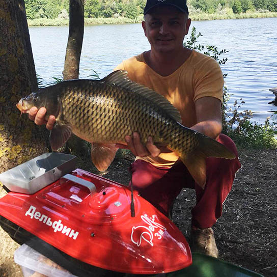 Трофейный карп на рыбалке и кораблик Дельфин фотография